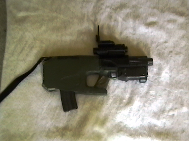CARB weapon on carbine mode. On top of the receiver is a red spot/laser designator. The magazine is an M16/M4 magazine.